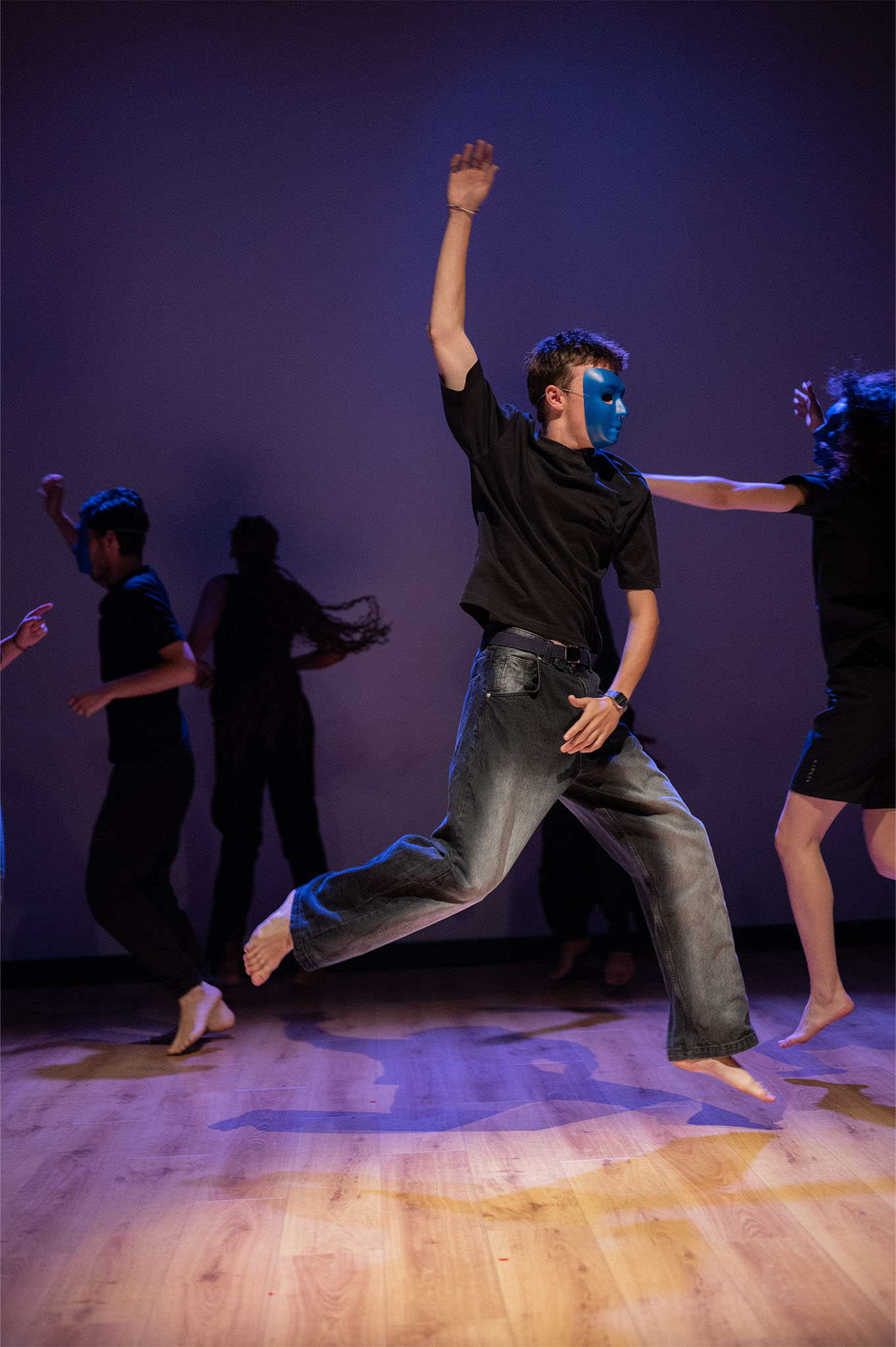 Au premier plan, un jeune garçon portant un masque bleu danse et saute, il semble comme suspendu dans les airs. En arrière plan, on aperçoit d'autres jeunes en train de danser.