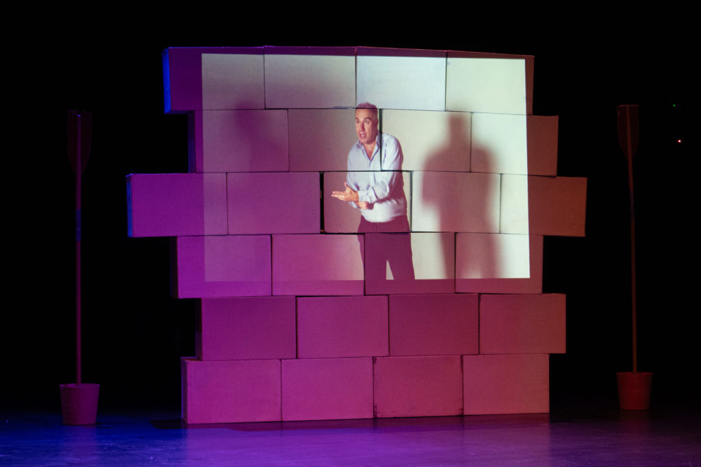 Vidéo-projection de François Gemenne sur un mur de parpaing éclairé en rose.